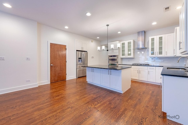 kitchen with dark countertops, visible vents, appliances with stainless steel finishes, a sink, and wall chimney range hood