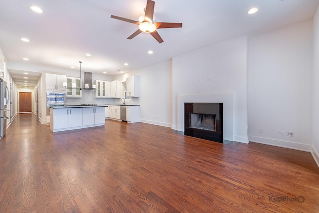 kitchen featuring dark countertops, wall chimney exhaust hood, open floor plan, stainless steel appliances, and white cabinetry