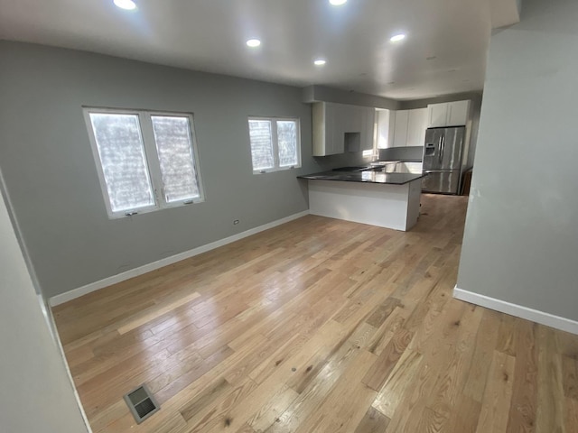 kitchen featuring stainless steel fridge with ice dispenser, dark countertops, a peninsula, light wood-style floors, and white cabinetry