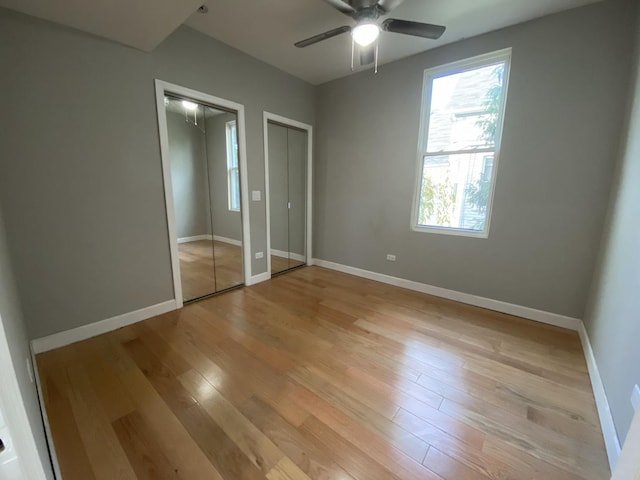 unfurnished bedroom featuring baseboards, two closets, a ceiling fan, and light wood-style floors