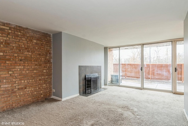 unfurnished living room with carpet, expansive windows, brick wall, a tile fireplace, and baseboards