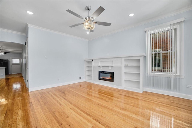 unfurnished living room with baseboards, a ceiling fan, a glass covered fireplace, hardwood / wood-style flooring, and crown molding