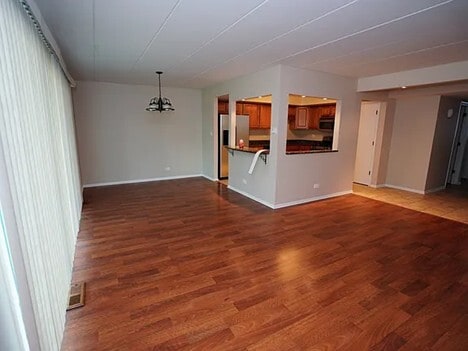 unfurnished living room featuring baseboards, dark wood finished floors, and a chandelier