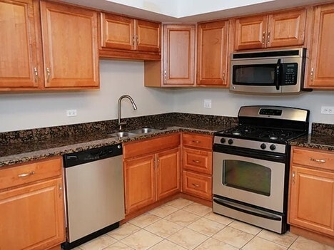 kitchen with stainless steel appliances, brown cabinets, a sink, and dark stone countertops