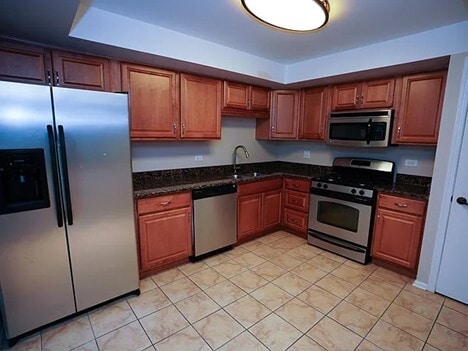 kitchen with brown cabinets, a tray ceiling, stainless steel appliances, and a sink