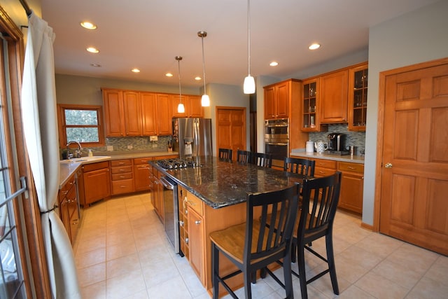 kitchen featuring a sink, a kitchen island, appliances with stainless steel finishes, a breakfast bar area, and brown cabinetry