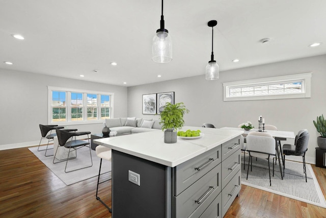 kitchen with gray cabinetry, a kitchen island, a breakfast bar, light countertops, and wood finished floors