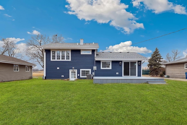 back of property with a lawn, roof with shingles, and a chimney