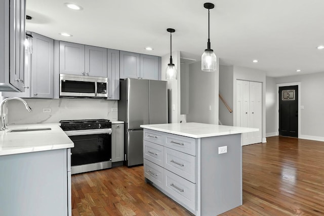 kitchen with a kitchen island, gray cabinets, wood finished floors, stainless steel appliances, and a sink