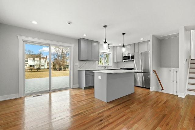 kitchen featuring a kitchen island, light countertops, gray cabinets, light wood-style floors, and stainless steel appliances