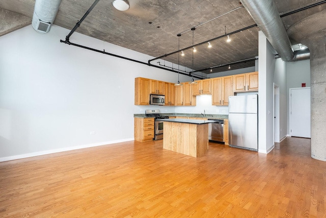 kitchen featuring stainless steel appliances, a sink, a towering ceiling, light wood-type flooring, and a center island