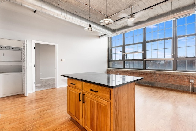 kitchen with a center island, stacked washer and dryer, dark countertops, hanging light fixtures, and light wood-type flooring