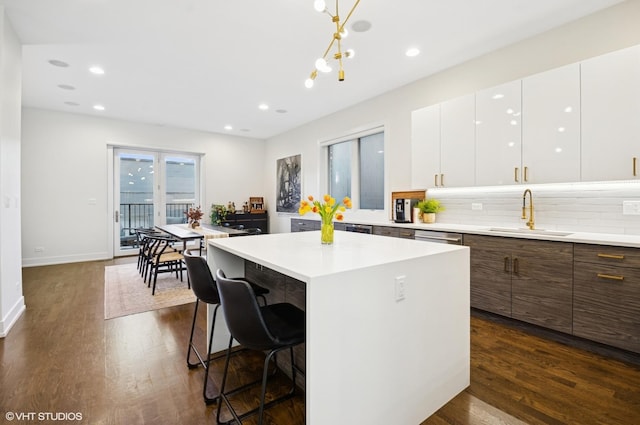 kitchen with dark wood-style floors, decorative backsplash, a center island, and a sink