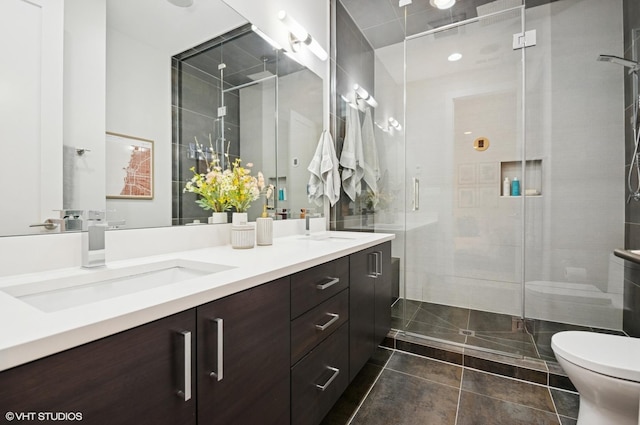 full bathroom with double vanity, a shower stall, toilet, and a sink