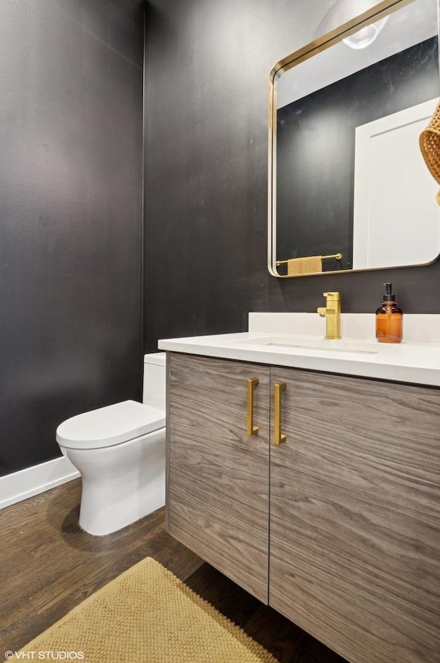 bathroom with vanity, toilet, wood finished floors, and baseboards