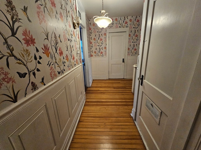 hallway featuring a wainscoted wall, wood finished floors, and wallpapered walls