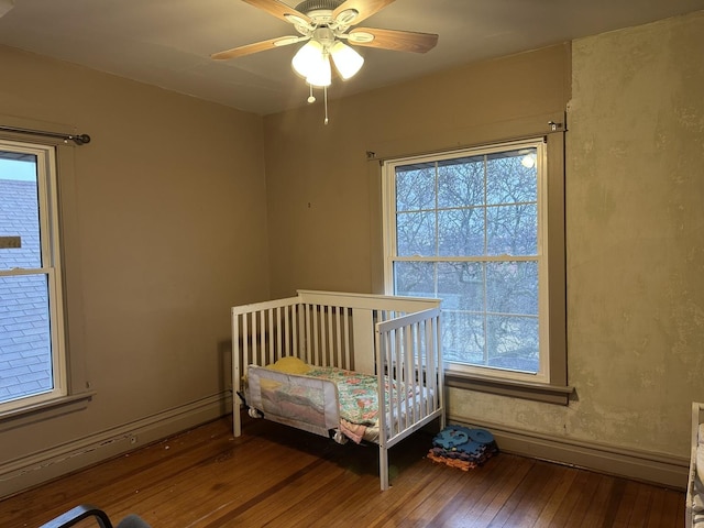 bedroom featuring ceiling fan, multiple windows, hardwood / wood-style flooring, and baseboards