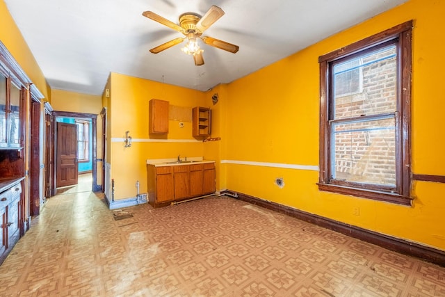 interior space with light floors, a sink, a ceiling fan, and baseboards