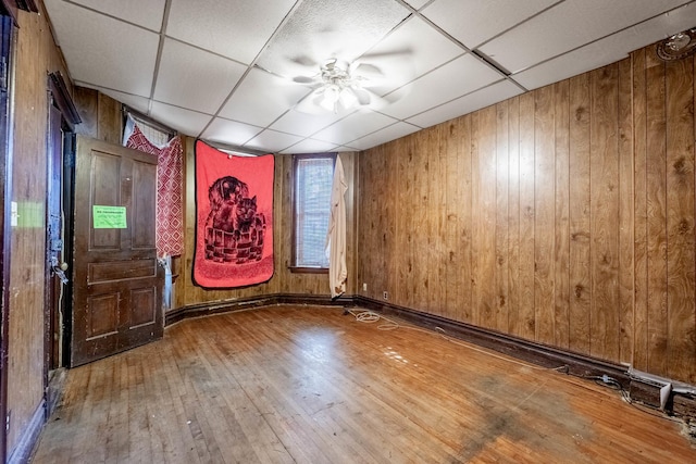 spare room featuring a paneled ceiling, wood-type flooring, wooden walls, and a ceiling fan