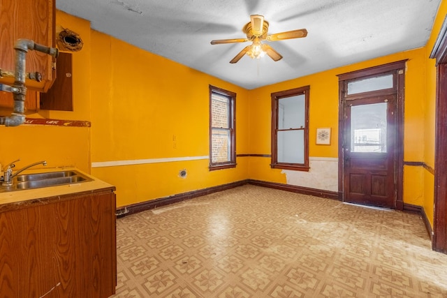 interior space with light floors, baseboards, a ceiling fan, and a sink