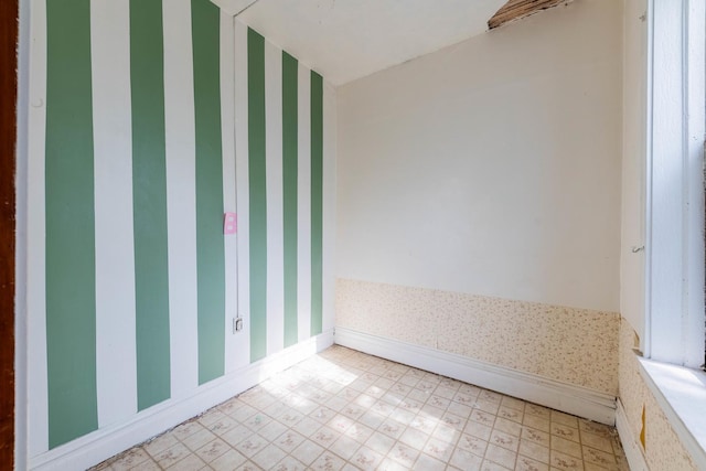 spare room with baseboards, light floors, and wallpapered walls