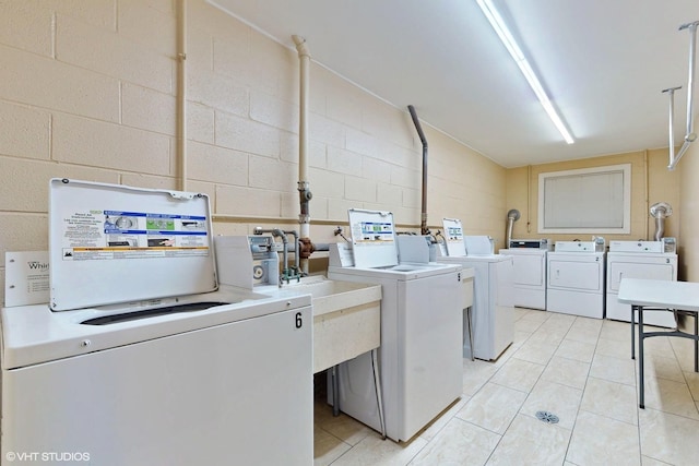 shared laundry area featuring concrete block wall, washing machine and dryer, and light tile patterned flooring