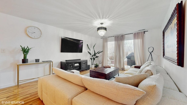 living area featuring light wood-style floors, baseboards, and an inviting chandelier