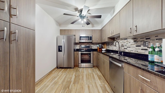 kitchen featuring tasteful backsplash, light wood-style flooring, appliances with stainless steel finishes, dark stone countertops, and a sink