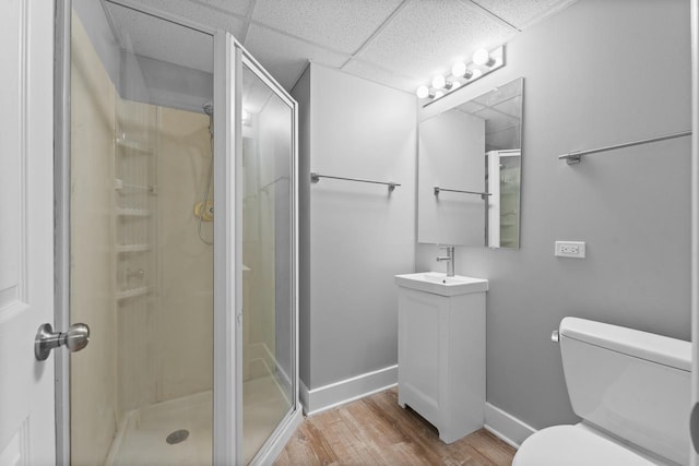 bathroom featuring baseboards, a drop ceiling, toilet, wood finished floors, and a shower stall