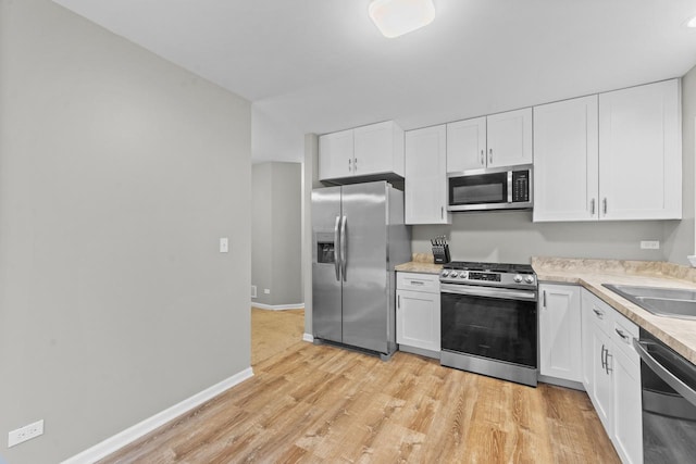 kitchen featuring baseboards, white cabinets, light wood-style flooring, stainless steel appliances, and light countertops