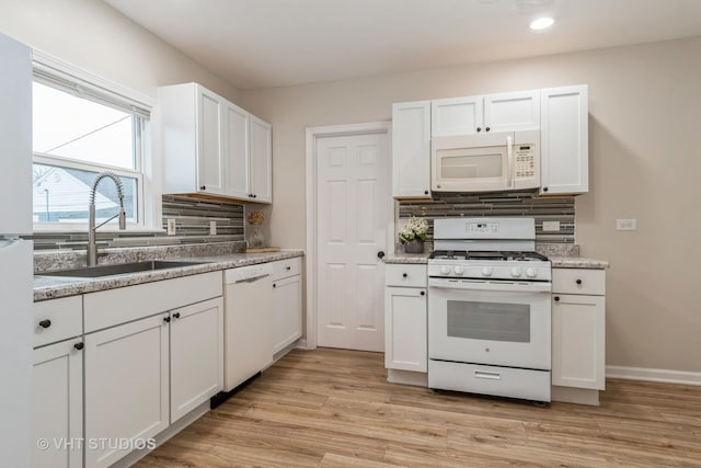 kitchen featuring white appliances, a sink, light wood-style floors, white cabinetry, and backsplash