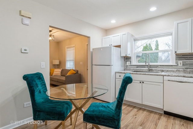 kitchen featuring light stone counters, light wood-style flooring, decorative backsplash, a sink, and white appliances