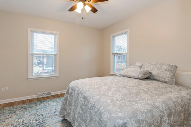 bedroom with a ceiling fan, visible vents, baseboards, and wood finished floors