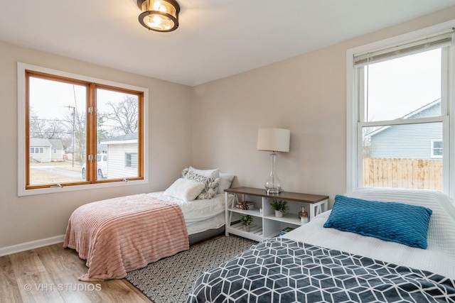 bedroom with multiple windows, wood finished floors, and baseboards