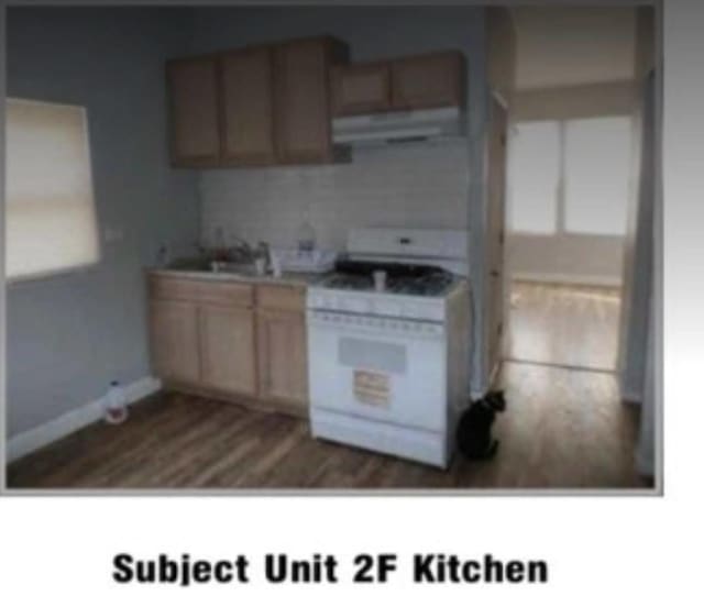 kitchen featuring white range with gas stovetop, a sink, exhaust hood, baseboards, and dark wood-style floors