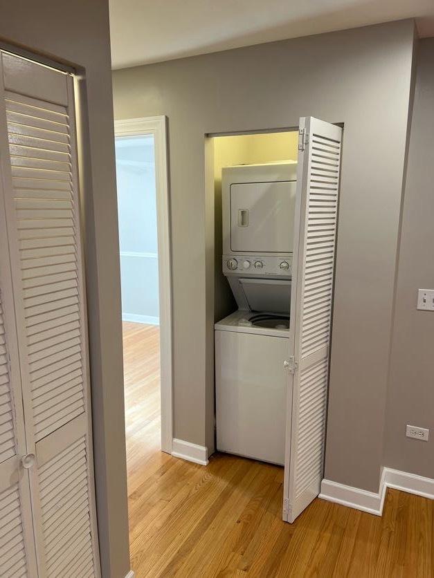 washroom with laundry area, baseboards, light wood finished floors, and stacked washer and clothes dryer