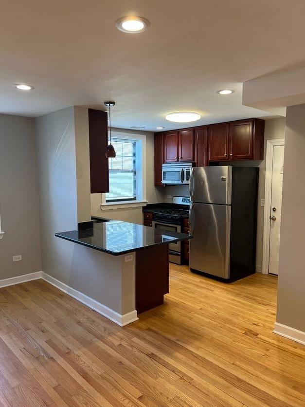 kitchen with appliances with stainless steel finishes, dark countertops, light wood-style floors, and baseboards