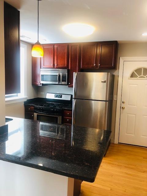 kitchen with dark stone countertops, hanging light fixtures, stainless steel appliances, dark brown cabinets, and light wood-style floors