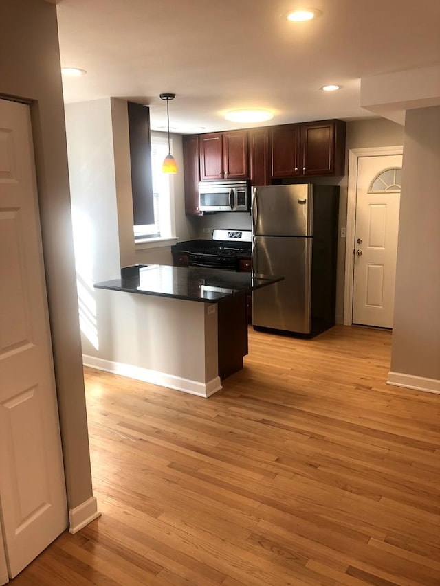 kitchen with stainless steel appliances, dark countertops, a peninsula, and light wood-style flooring