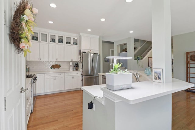 kitchen with a peninsula, light wood finished floors, tasteful backsplash, and appliances with stainless steel finishes