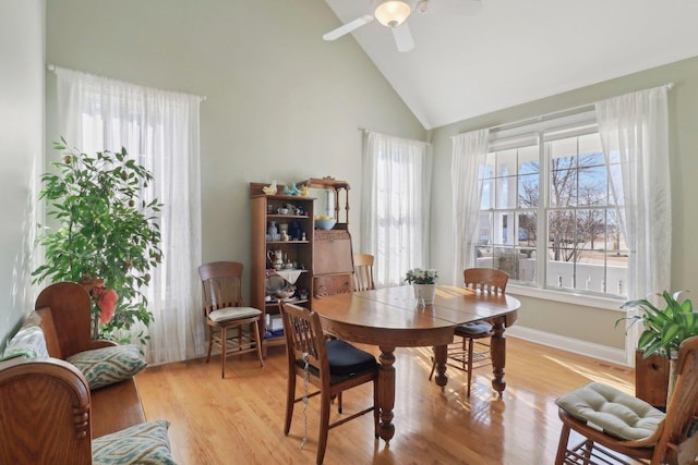 dining space featuring a ceiling fan, baseboards, light wood finished floors, and high vaulted ceiling