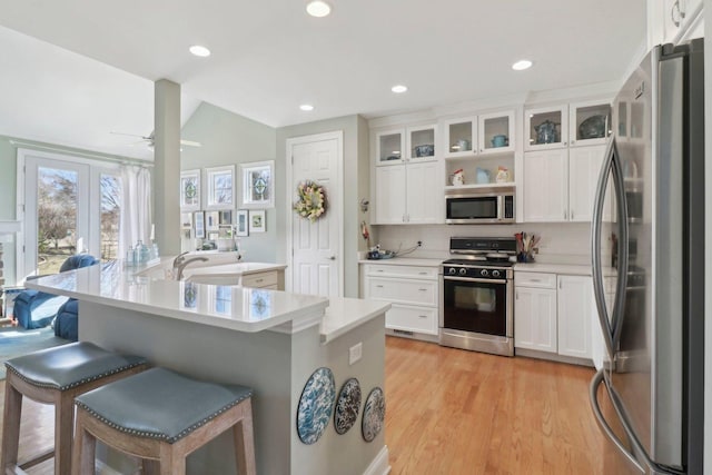 kitchen with light wood finished floors, a breakfast bar area, appliances with stainless steel finishes, white cabinets, and a ceiling fan