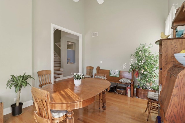 dining room featuring visible vents, baseboards, stairs, light wood-type flooring, and a towering ceiling