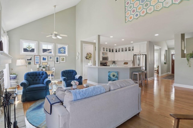 living room with baseboards, light wood-style flooring, a fireplace, high vaulted ceiling, and a ceiling fan