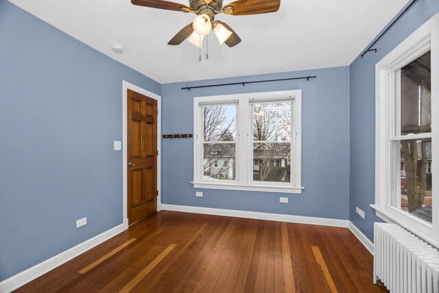 empty room with radiator heating unit, baseboards, ceiling fan, and wood finished floors