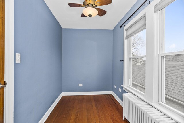 spare room featuring radiator, ceiling fan, baseboards, and dark wood-style flooring