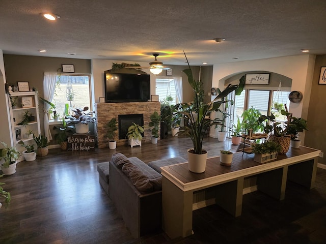 living area with a healthy amount of sunlight, a stone fireplace, a textured ceiling, and wood finished floors