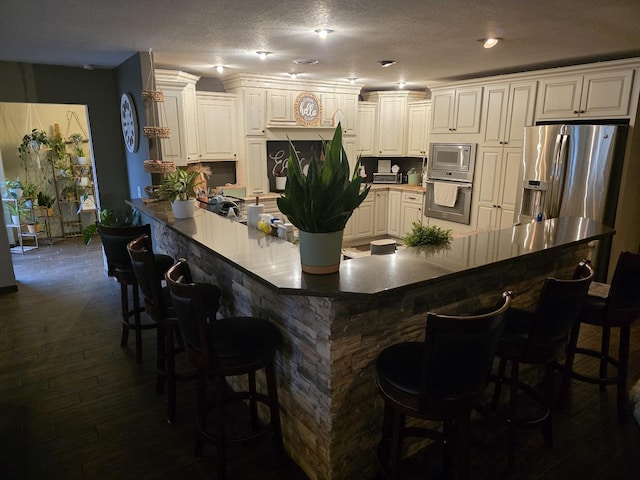 kitchen with dark wood-style floors, a peninsula, appliances with stainless steel finishes, and a breakfast bar area