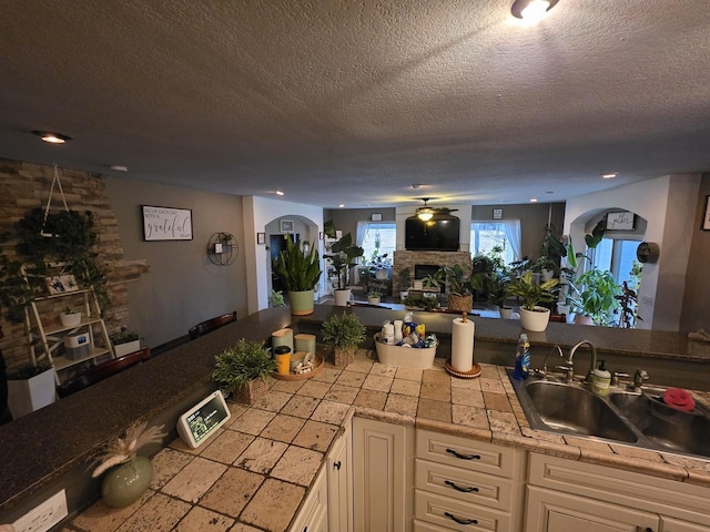 kitchen with arched walkways, a fireplace, a sink, white cabinets, and open floor plan