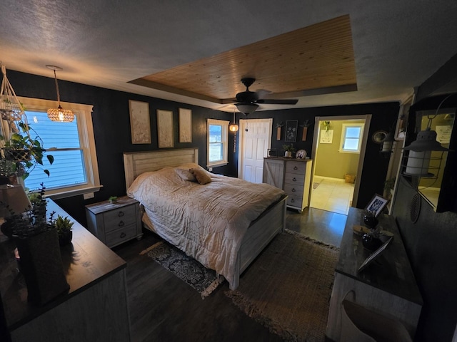 bedroom with a textured ceiling, connected bathroom, dark wood-style flooring, a ceiling fan, and a raised ceiling